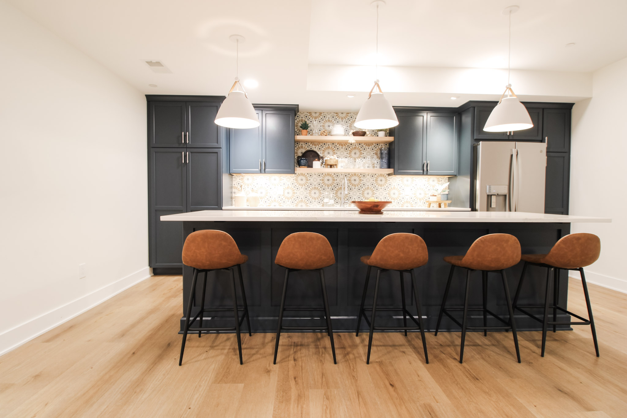 Basement bar area with seating, patterned backsplash, and modern finishes.